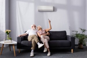 senior-citizen-couple-on-sofa-in-living-room-changing-temperature-of-mini-split-with-remote